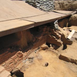 Brick ovens, postholes, and additional features within a half-covered excavation unit lined with sandbags