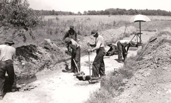 Black and white photograph of excavators working along a road