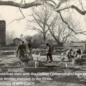 black and white photograph of men excavating with shovels and wheelbarrows in front of brick house ruins