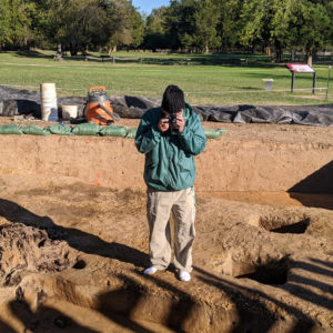 photographer standing in an excavation unit and taking a picture