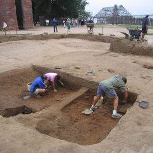 Two archaeologists excavating on either side of a unit balk