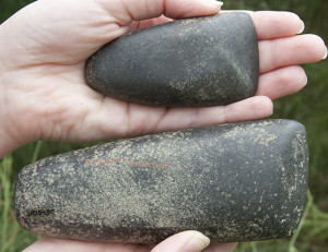 Hands holding two rounded stone celts