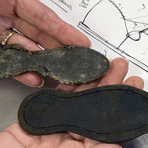 Researcher holding two leather shoes in front of measured drawing