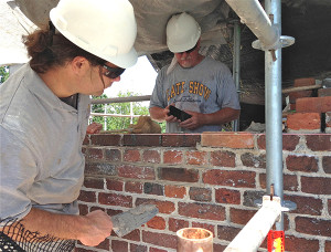 two craftsmen wearing hardhats building a brick wall