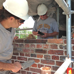 two craftsmen wearing hardhats building a brick wall