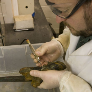 Conservator using a tool to remove corrosion on a pistol grip
