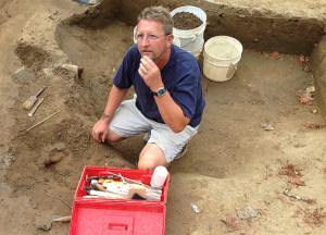 Conservator kneeling with a tool case next to an iron artifact in situ