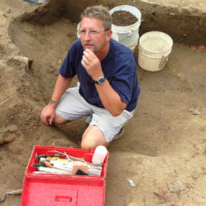 Conservator kneeling with a tool case next to an iron artifact in situ