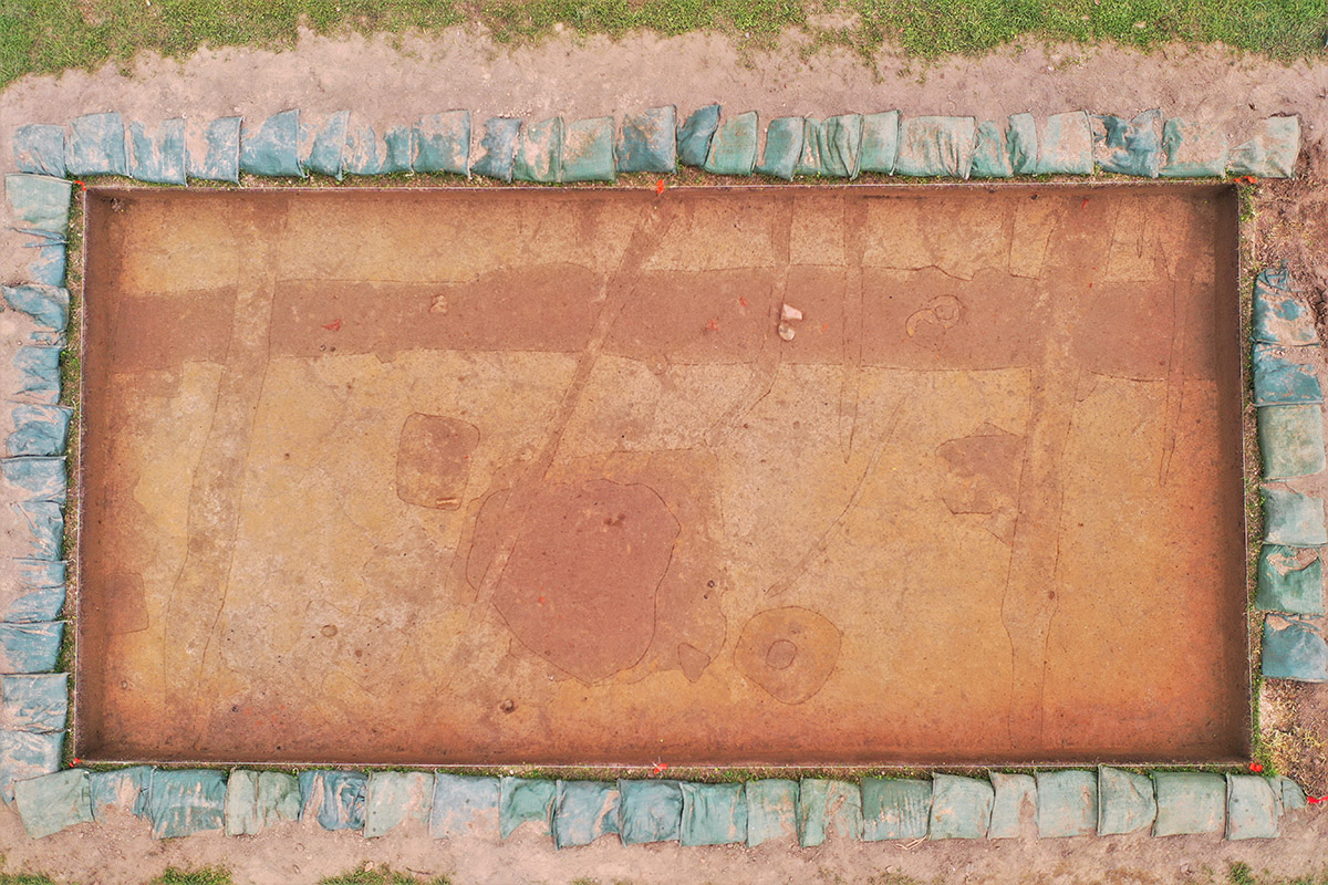 Two adjacent squares in the north field. The features have been scored to make them more visible. One of the pit features is the dark stain near the center. Several postholes are visible and the east/west ditch can be seen running horizontally near the top of the squares. Multiple cobbles and bricks are can be seen poking out of the ditch. Plow scars are visible running roughly north/south.
