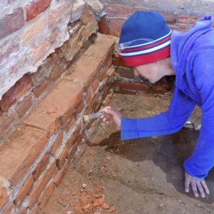 Archaeologist cleaning mortar in a brick wall