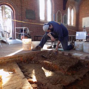 Archaeologist trowels in unit inside brick church