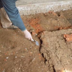 Archaeologist points with trowel to excavated mortar pad