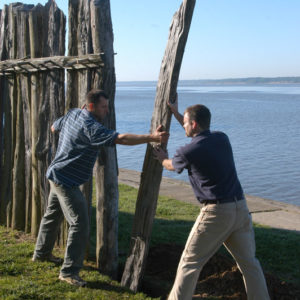Two people raise a timber post at the end of a partial wall