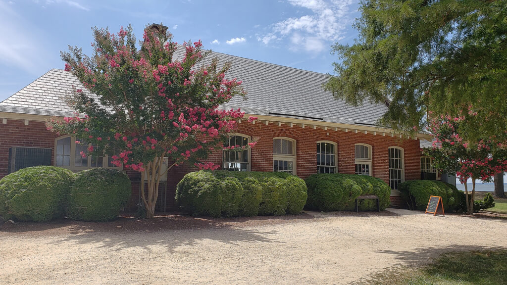 The Dale House is a one-story brick building with boxwoods and a pink crape myrtle tree in front of it
