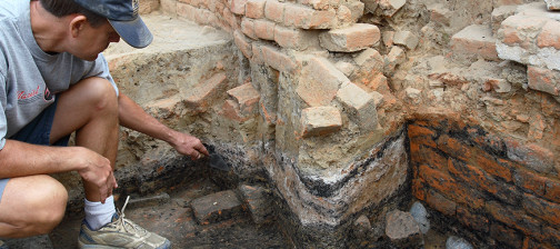 Archaeologist pointing to ash layer in unit wall