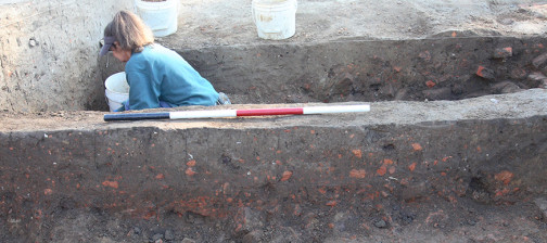 Archaeologist excavating on other side of unit wall