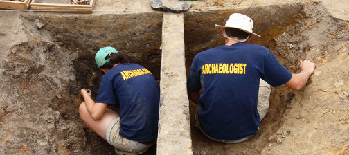 two archaeologists excavate on either side of a balk in the middle of a unit