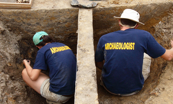 two archaeologists excavate on either side of a balk in the middle of a unit