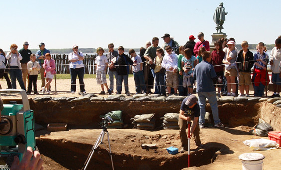 Archaeologist records unit with total station while another talks to a large group