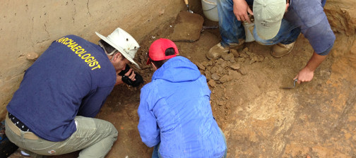 Archaeologist video recording excavations while others trowel nearby