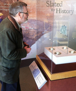Man examines an inscribed piece of slate in a museum case