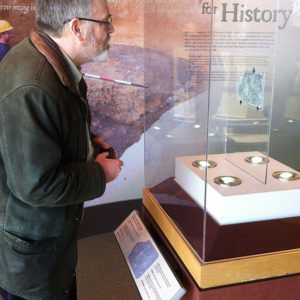 Man examines an inscribed piece of slate in a museum case