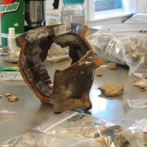 Mended earthenware pipkin and assortment of other ceramic sherds on a lab table