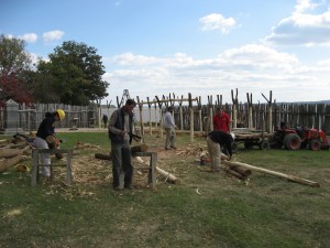 Crew sawing wooden posts in front of standing Y-shaped posts of a building frame