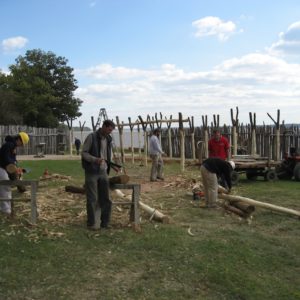 Crew sawing wooden posts in front of standing Y-shaped posts of a building frame
