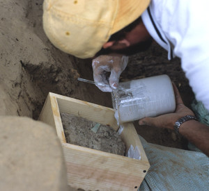 Conservator using a tool to spoon solution from a glass container onto an artifact in a wooden tray