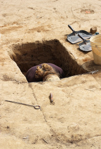 A student excavating in a deep square feature