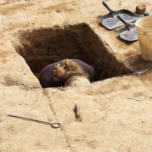 A student excavating in a deep square feature