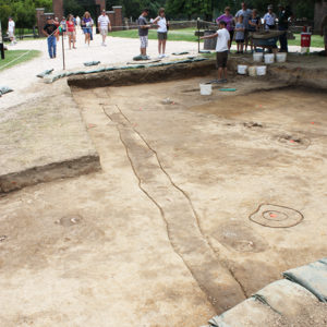excavation unit with a variety of features and a student talking to a group of visitors in the background