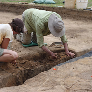 Two students using trowels to excavate a feature