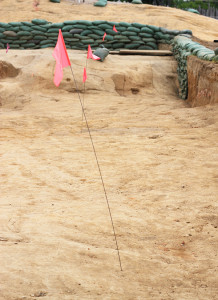Flags marking a feature within a large excavation area lined with sandbags