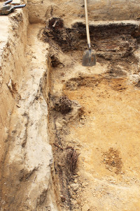 portions of wooden posts along the sides of an excavation unit and a shovel standing along the opposite edge