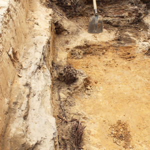 portions of wooden posts along the sides of an excavation unit and a shovel standing along the opposite edge