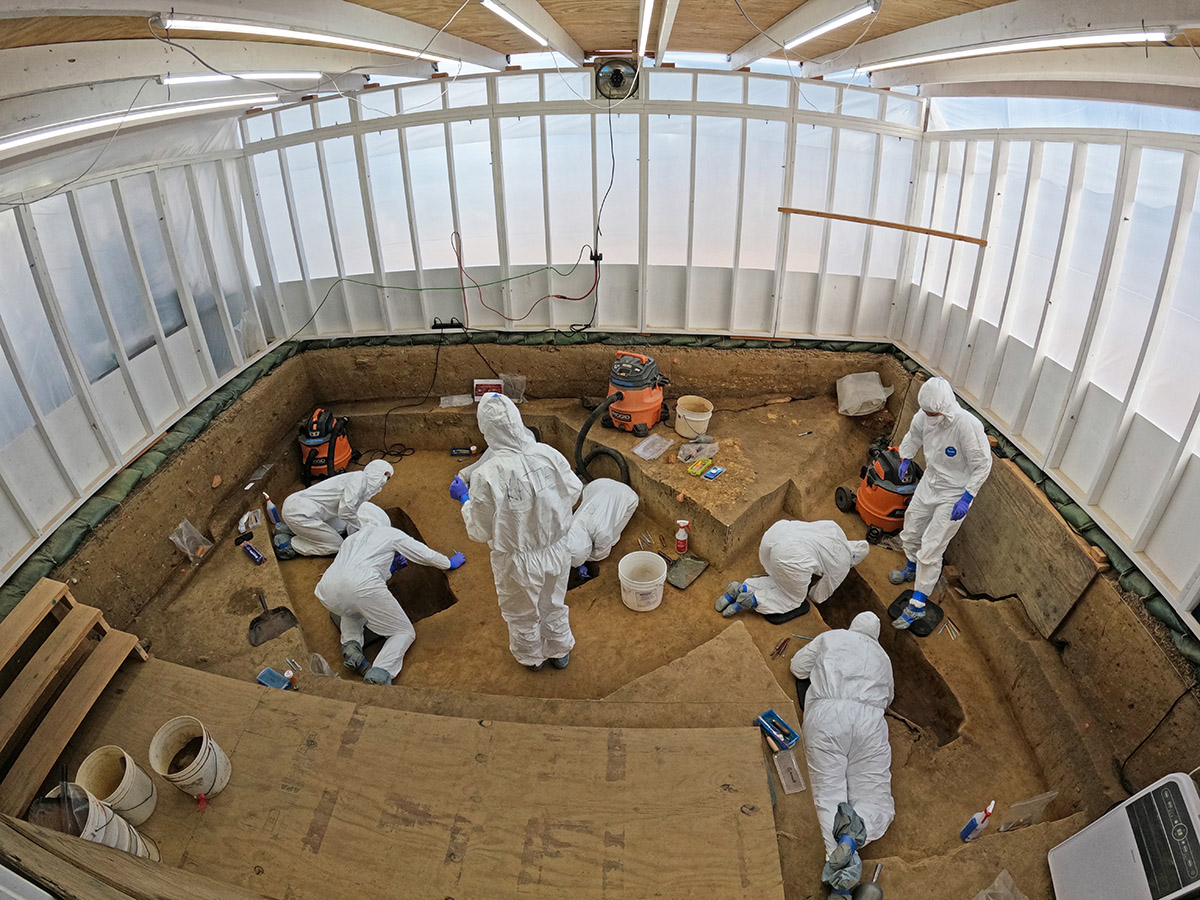 The archaeological team works inside the 1607 Burial Ground. The team writes their names on the back of their Tyvek suits because identification is difficult otherwise. Human remains have been digitally removed from the photo.