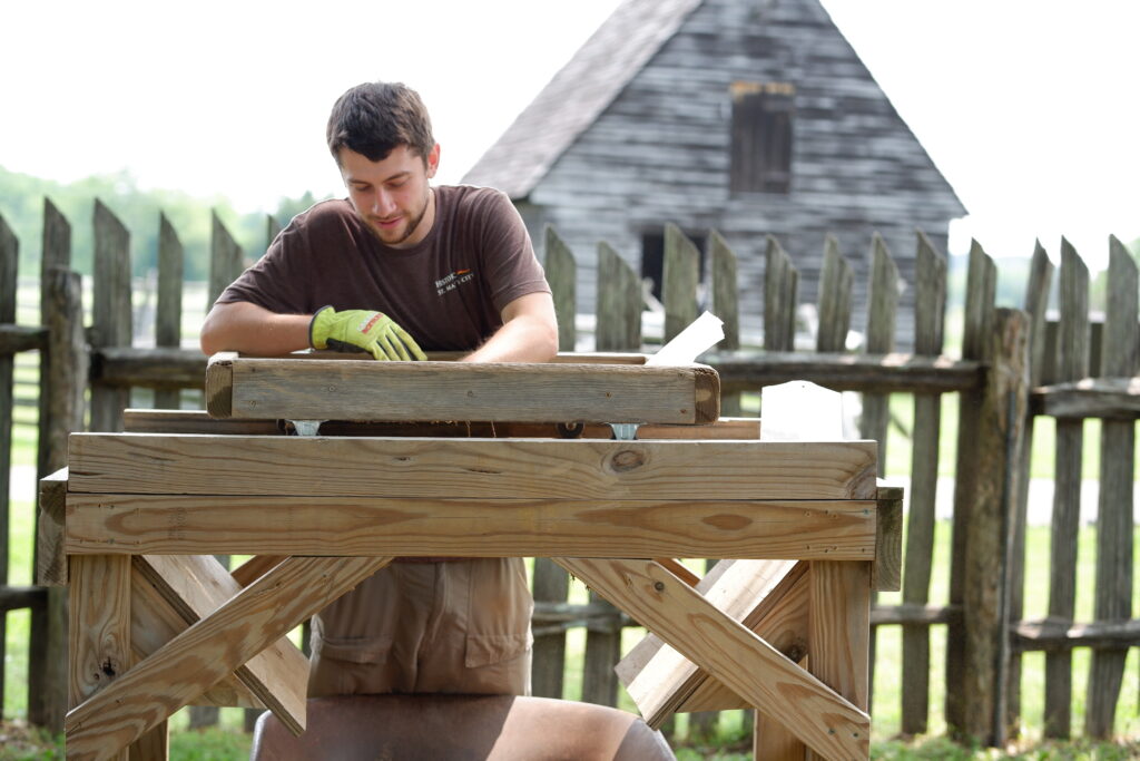 An archaeologist screens for artifacts in front of a reconstructed 17th century building at Historic St. Mary's City