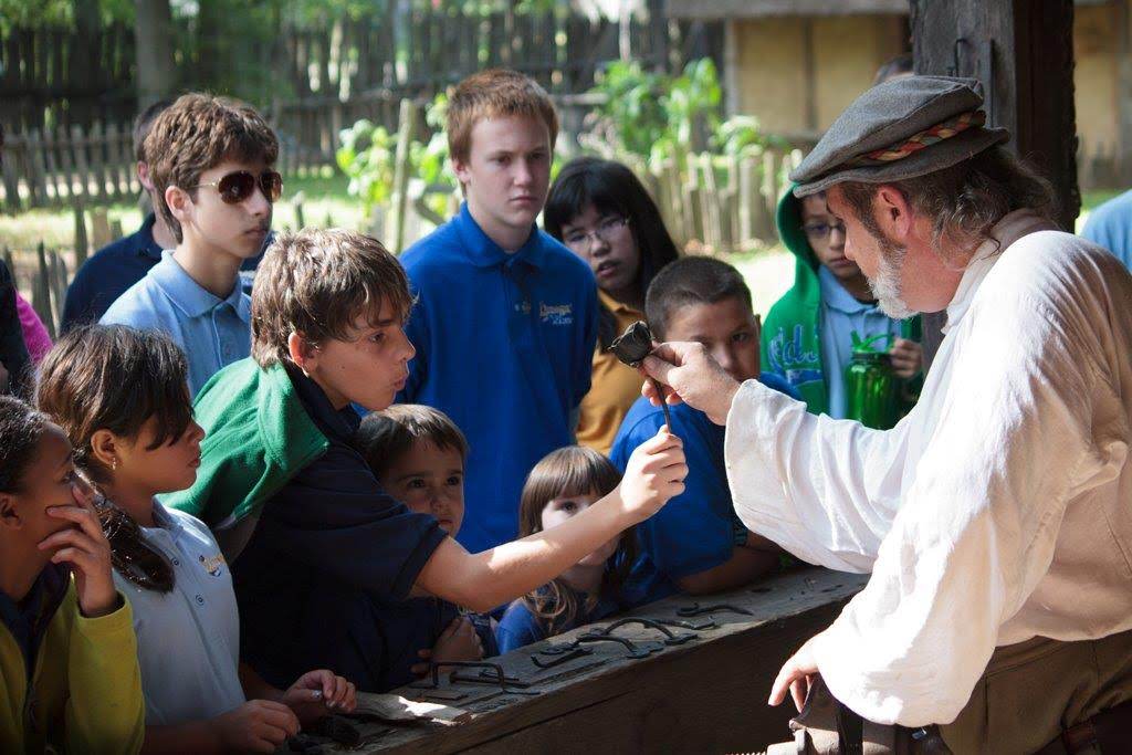 A group of young boys gather around a blacksmith at Henricus Historical Park