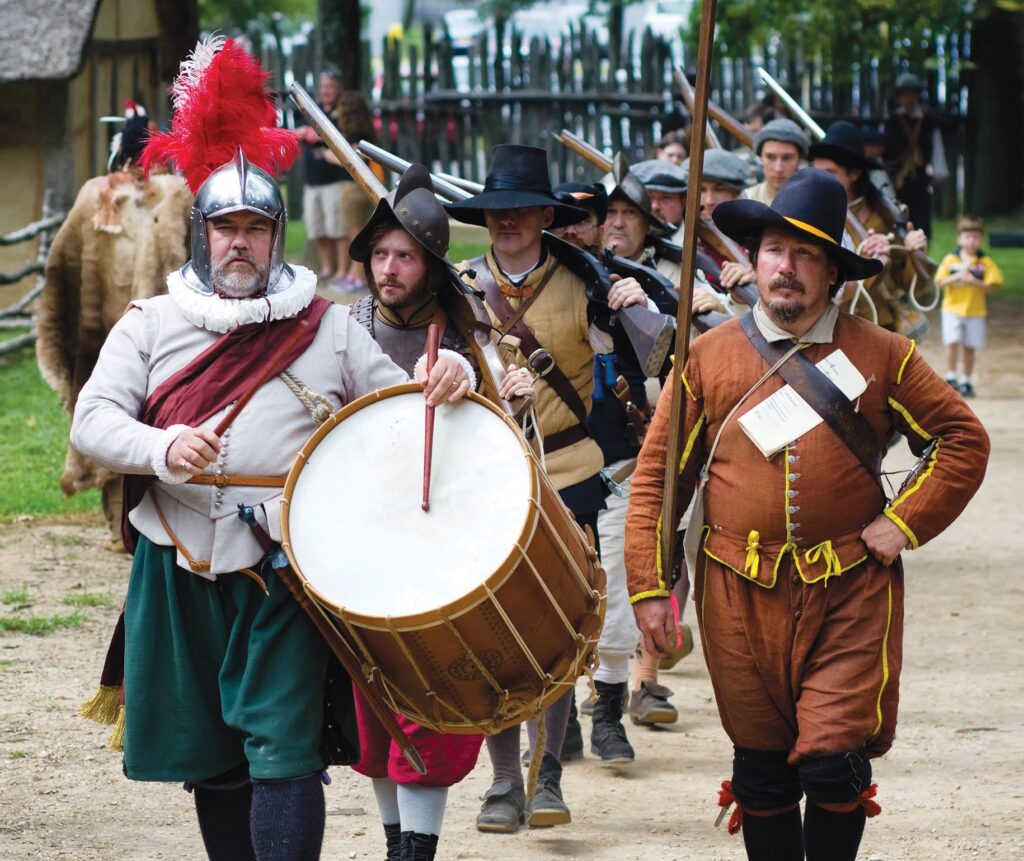 Men wearing 17th century clothes march down a road at Henricus Historical Park
