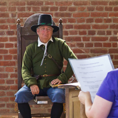 Man in historical clothing listening to a visitor read from a paper
