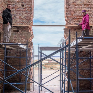 Two staff members stand on a scaffold on either side of a church doorway