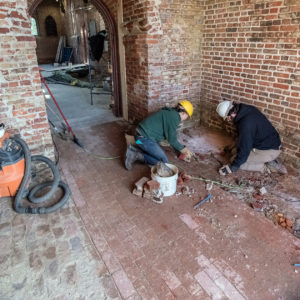 Two archaeologists excavate the floor of a brick church tower