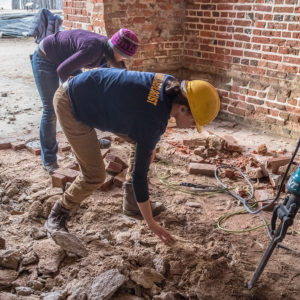 Archaeologists use a jackhammer to excavate the floor of a brick church tower