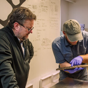 Conservator Dr. Chris Wilkins and Senior Staff Archaeologist Sean Romo examine the cask staves that lined a mid 17th-century well for marks that might give insights into who made them or what they originally contained.