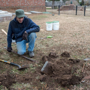 Conservator using a pole to lift a buried gravestone fragment