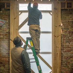 Two staff install wooden door in brick tower