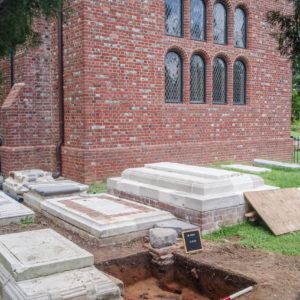 Excavation unit next to tombstones in a graveyard in front of a brick church