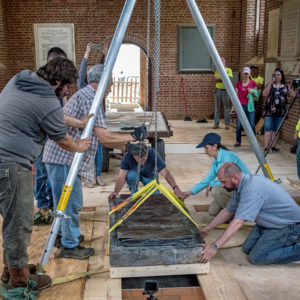 Archaeologists lower the granite tombstone into the church floor using tripod